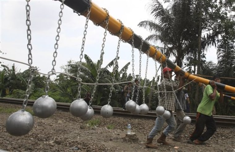 Workers install a frame with concrete balls suspended on it above railway tracks in Bekasi, West Java, Indonesia, Tuesday.